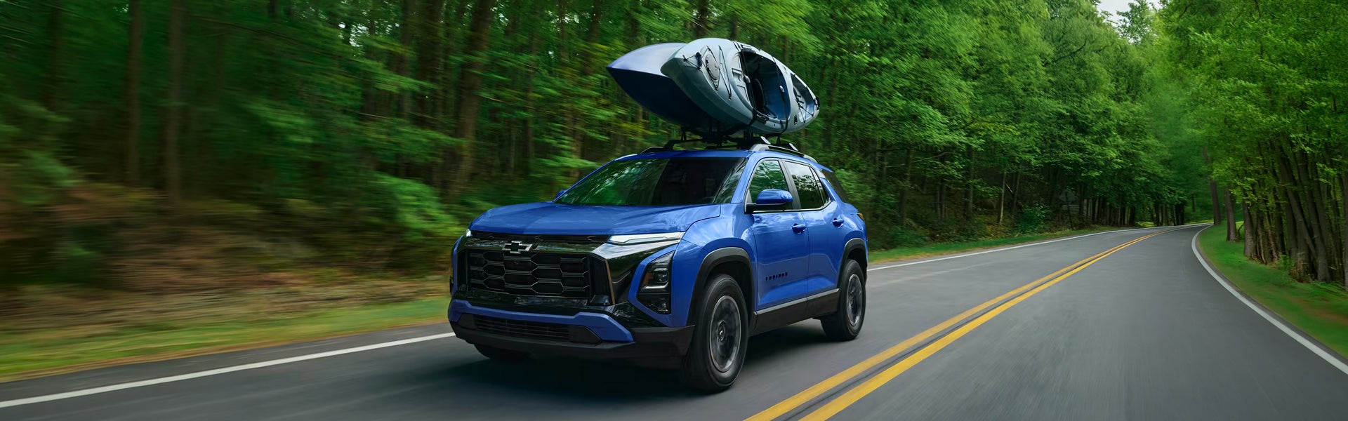 Blue Chevrolet Equinox driving through a forest with kayaks on top